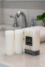 Unscented white candles on a bathroom counter with visible labels.