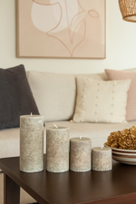 Set of four scented candles on a coffee table with a couch and decorative elements in the background.