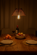 Dining table setting with fruit, wine, and a hanging light bulb in a warmly lit room.