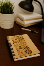 MDF diary with floral design on a wooden surface with books and a plant in the background.