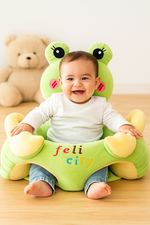 Child sitting on a green frog-shaped cushion surrounded by toys.