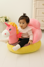 Child sitting on a pink and yellow unicorn-shaped sofa seat in a room with white flowers and a dresser.