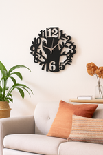 Decorative bird wall clock on a wall above a sofa with pillows and a plant.