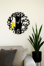 Decorative wall clock with a yellow bird on a white wall above a sofa with cushions and a plant.