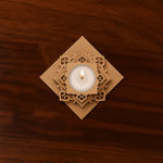 Decorative square-shaped MDF Chatushpad tealight holder with a lit candle in the center on wooden background