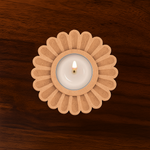 Laser-cut MDF daisy flower-shaped tealight holder with a lit candle in the center on a polished wooden surface