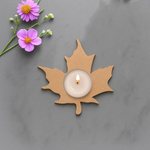 Laser-cut leaf-shaped MDF tea-light candle holder with lit tealight on gray background with purple flowers