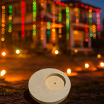 Round MDF T-Light Candle Holder placed outdoors with glowing festive lights in the background