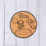 Round wooden cutout with space-themed design and 'Kian' engraved, on a light wooden background.
