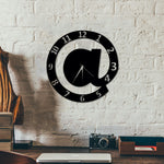 Stylish black alphabet wall clock with "@" design, made from 3mm MDF board, featuring white numerals and a quartz mechanism, mounted on a white brick wall in a modern workspace