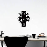 Tree wall clock featuring a black design with cut-out branches, leaves, and numbers, mounted on a white wall above a modern desk setup with books and decor.
