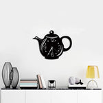 A stylish kettle-shaped wall clock in black, mounted on a white wall above a modern console table with decor accents.