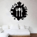 Black wall art featuring a circular design with a fork, spoon, and knife at the center, surrounded by silhouettes of kitchen utensils and dining-related items, mounted on a white brick wall above a white sofa.