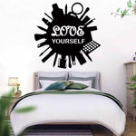 Black self-love wall art featuring the phrase 'LOVE YOURSELF' surrounded by silhouettes of beauty and self-care items, mounted above a modern bed in a cozy bedroom.