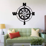 Black wall art featuring a compass design with cardinal directions (N, S, E, W), mounted on a white wall above a light green sofa with colorful cushions, in a modern living room setting