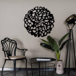 Black circular MDF wall art with an abstract cutout design, mounted on a neutral wall, enhancing a modern living space with elegant furniture and decor.