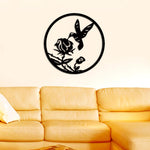 Circular hummingbird wall art in black featuring a bird hovering near a rose, mounted on a beige wall above a yellow sofa.