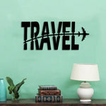 Black MDF wall art with the word "TRAVEL" and an airplane design cutting through it, mounted on a light green wall above a table with books, a lamp, and decor items.