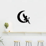 Black MDF moon fairy wall decor featuring a delicate silhouette of a fairy sitting on a crescent moon holding a star, mounted on a white wall above a minimalist shelf and stools.