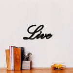 Black MDF wall art featuring the word "Live" in elegant cursive typography, mounted on a white wall above a wooden surface with books, a glass vase, and a bowl with yellow flowers.