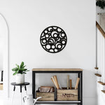 Circular black MDF wall art with abstract cutout patterns of overlapping circles, mounted on a white wall above a rustic wooden console in a modern hallway