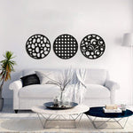 Set of three circular black MDF wall art pieces with abstract cutout designs, mounted on a white wall above a modern sofa in a contemporary living room setting.
