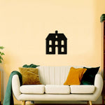 Black home-shaped wall art featuring a minimalist house design, mounted on a beige wall above a white sofa with colorful throw pillows.