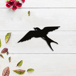 Black flying bird wall decor featuring a silhouette of a bird mid-flight, displayed on a white wooden background with scattered leaves and flowers.