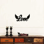 Black MDF wall art featuring the word "Love" with wings on either side, mounted on a light-colored wall above a rustic wooden console with decorative items