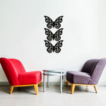 Unique butterfly wall art featuring a set of four intricately designed black butterflies mounted on a white wall between red and gray chairs with a round table.