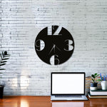 Modern MDF digits wall clock with a sleek black circular design and cut-out numbers, mounted on a white brick wall above a wooden desk with a laptop and potted plants.