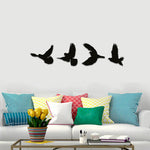 Black free flying birds wall decor featuring silhouettes of four birds in flight, mounted on a wall above a colorful sofa with vibrant cushions.