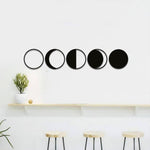 Minimalist moon phase wall art displayed on a white wall above a wooden shelf and stools.