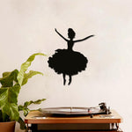 Black silhouette of a dancing girl wall decor featuring a graceful ballerina design, mounted on a beige wall above a vintage record player and a green potted plant.