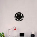 Black minimalist wall clock with bold numerals and circular accents, mounted on a plain wall above a modern desk setup.