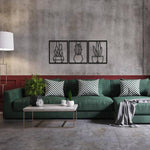 Black plant wall art featuring three framed designs of potted plants, mounted on a textured wall above a green sofa with checkered cushions.