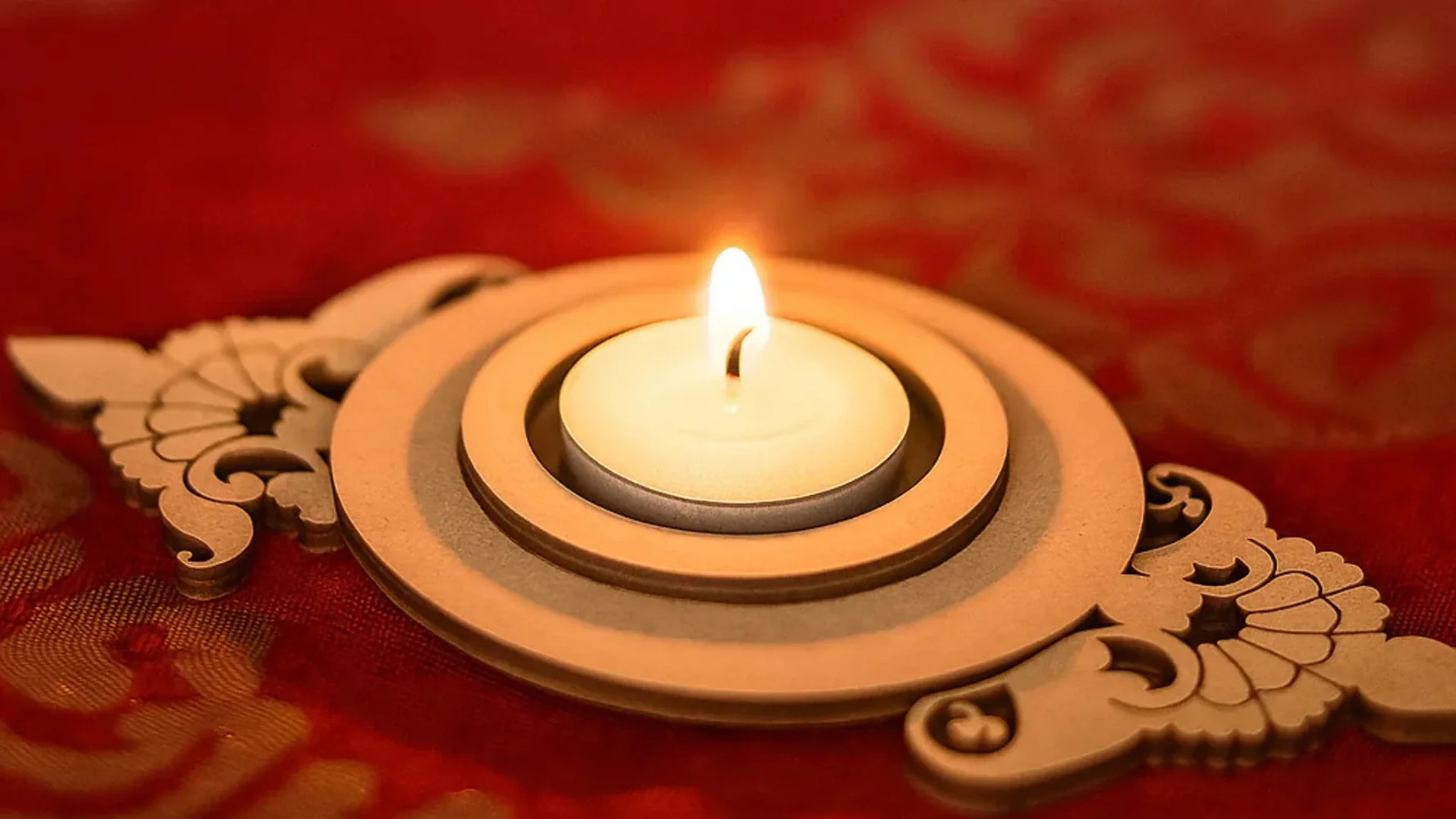 DIY MDF floral tealight candle holder with lit candle on red festive background.