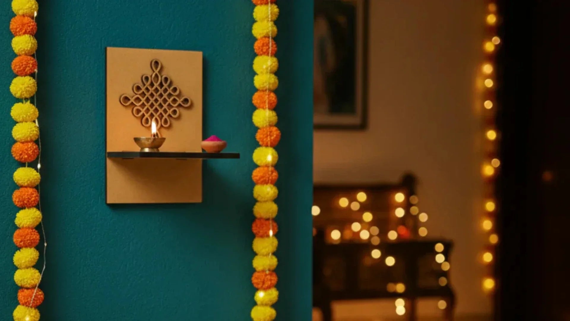 Minimalist MDF wall-mounted pooja shelf with an engraved Kolam design, decorated with a lit diya and festive marigold garlands on a teal wall, creating a warm Indian home décor setting.