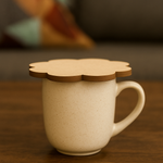 Beige ceramic mug with a flower-shaped MDF coaster used as a lid, placed on a wooden table.
