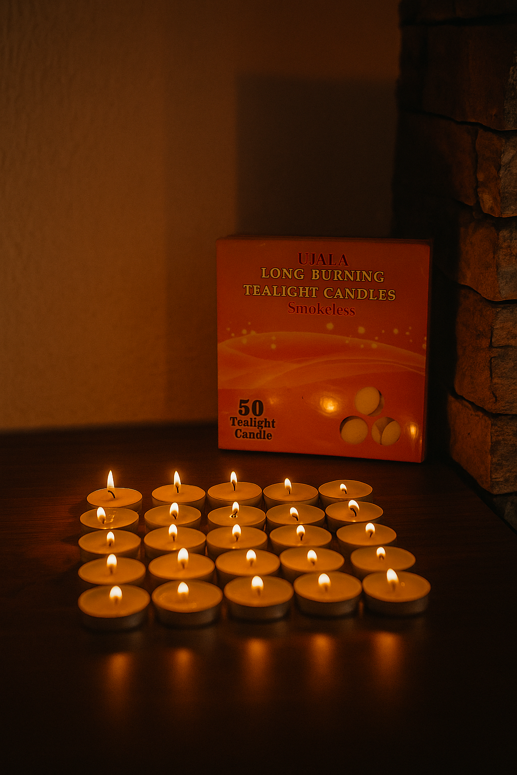 Lit tealight candles arranged in rows on a wooden surface with a box labeled 'Ujala Long Burning Tealight Candles Smokeless – 50 Tealight Candle' in the background