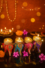 Decorative elephant candle stand with colorful fabric on a reflective surface, with a warm, blurred background.