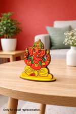 Colorful MDF DIY Ganesha statue on a wooden table with a red wall and plants in the background.