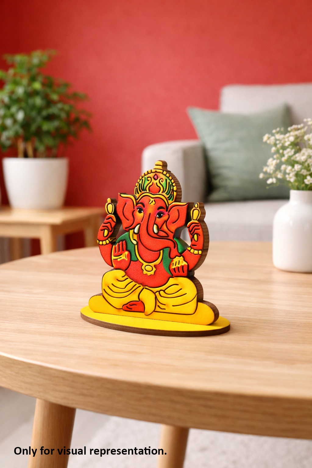 Colorful MDF DIY Ganesha statue on a wooden table with a red wall and plants in the background.
