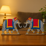 Two decorative mdf elephant figurines with colorful blankets on a wooden surface.