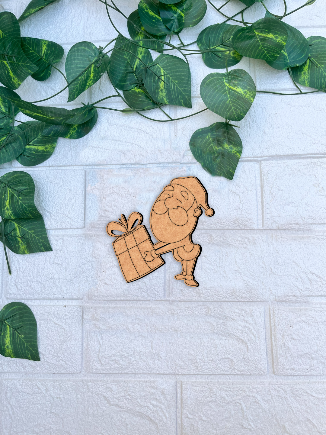 DIY MDF Santa Claus cutout holding gift for Christmas craft mounted on a white textured brick wall