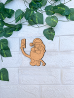 DIY MDF Santa Claus cutout taking selfie for Christmas craft mounted on a white textured brick wall