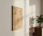 Abstract line art of a face on a wooden panel hanging on a wall with natural light.