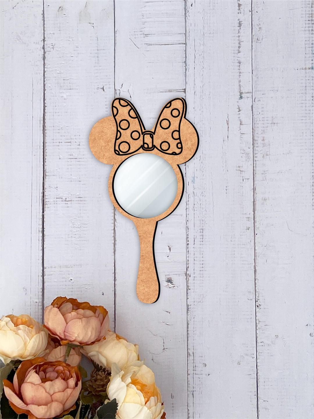 Handheld mirror with Minnie Mouse ears and bow on a light wooden background