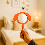 Hand holding a red-painted dog-ear shaped MDF mirror in a cozy bedroom