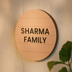 Round MDF board sign with 'SHARMA FAMILY' text on a wall.